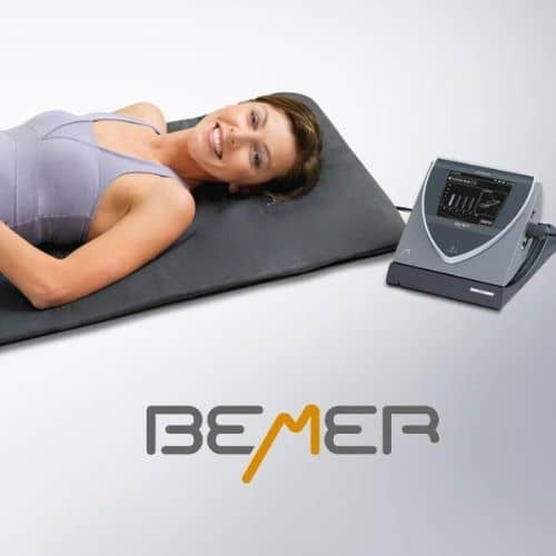 Woman lying on BEMER Pro-Set full-body PEMF mat with control unit beside her