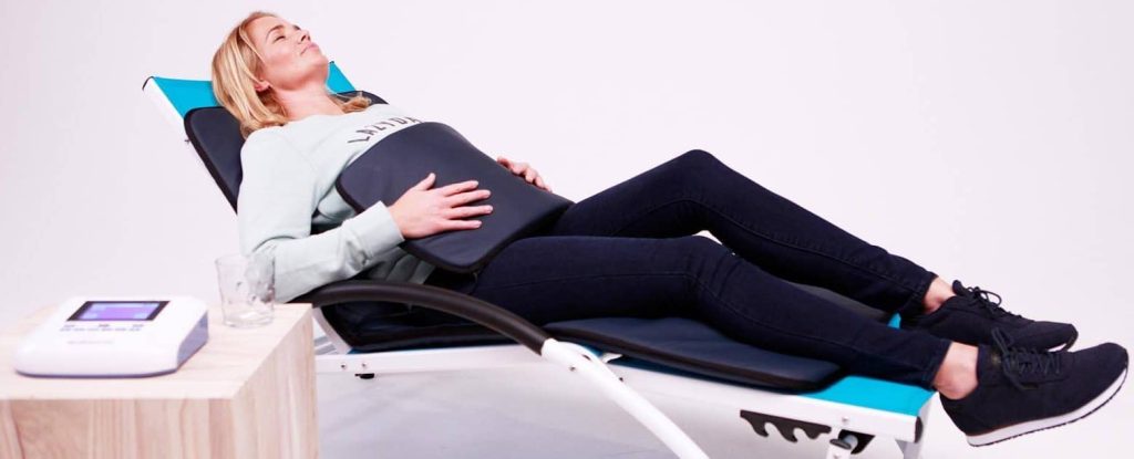 Woman seated on lounge chair using BioBalance PEMF mat with controller on side table