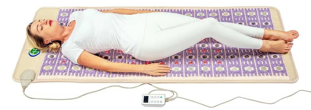 Woman lying on HealthyLine TAJ PEMF mat with controller beside her