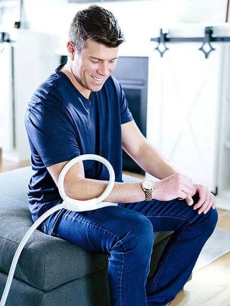 Man using Magnawave Mini PEMF coil applicator on elbow while seated on sofa