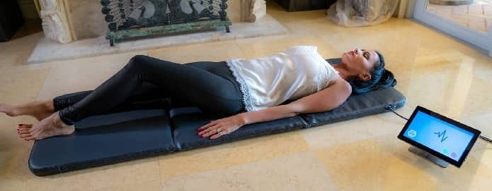 Woman lying on iMRS Prime full-body PEMF mat with control unit beside her