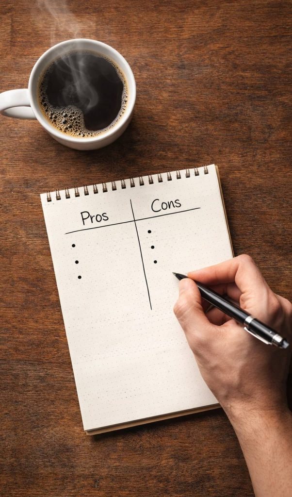 Overhead view of notebook with pros and cons list beside a steaming cup of coffee, representing decision-making before buying a PEMF device